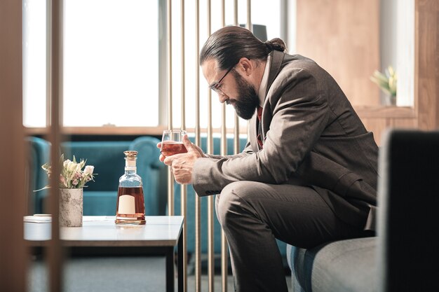 Problemas en el trabajo. Hombre barbudo de pelo oscuro que se siente fatal después de problemas en el trabajo y beber alcohol