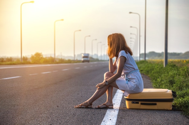 Probleme bei der Fahrt. das Mädchen sitzt auf einem gelben Koffer am Straßenrand