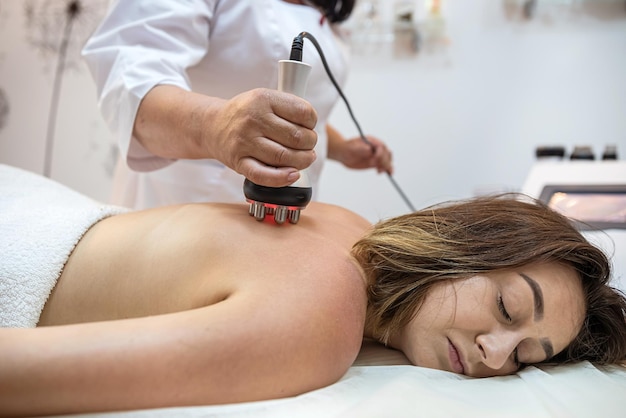 Procedimento de cuidado corporal de mulher deitada em lençóis brancos, uma massagista massageia cliente do sexo feminino no salão