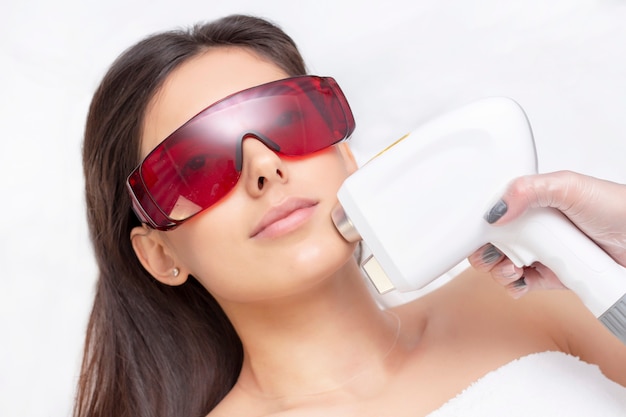 Procedimento de fotoepilação no salão de beleza. jovem mulher recebendo tratamento a laser de depilação no rosto no centro de beleza de perto
