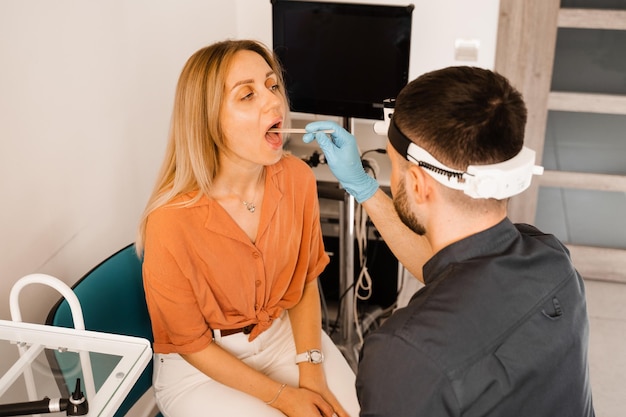 Procedimento de orofaringoscopia Otorrinolaringologista examina a garganta da mulher com espátula Consulta com laringologista