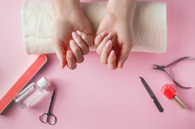 Procedimento de spa para cuidados com as unhas em um salão de beleza mãos femininas e ferramentas para manicure em fundo rosa