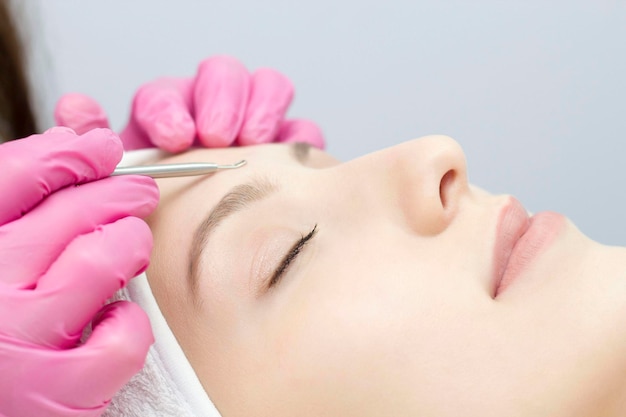 Procedimento para limpar a pele com ferramenta de aço de cravos e acne Limpeza profunda do rosto feminino com removedor de cravo no salão de beleza Cosmetologista recebendo terapia de limpeza