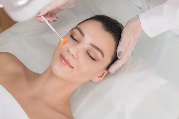 Foto procedimiento cosmético peeling químico mano del médico con un cepillo tocando la cara de una mujer