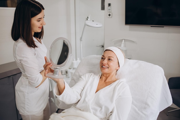 Procedimiento estético Esteticista aplicando máscara facial de arcilla en la cara de una mujer de mediana edad sonriente mujer atractiva madura disfrutando de un tratamiento de cuidado de la piel antienvejecimiento en el estudio de cosmetología