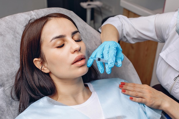 Procedimiento de levantamiento. Una niña se acuesta en una silla y se hace un aumento de labios con rellenos. Cuidando de ti y de la belleza.