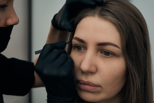 Procedimiento de maquillaje permanente de cejas. Tatuaje de cejas, proceso. El uso de herramientas por parte de un maestro para el maquillaje permanente de cejas.