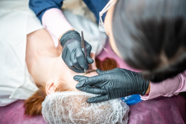 Procedimiento de microblading de cejas un maestro en guantes negros está haciendo una aguja de mezcla de cejas de modelos