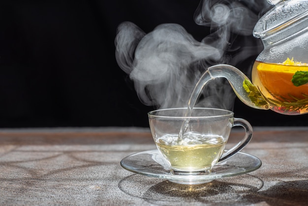 Procese la preparación del té, humor oscuro. El vapor del té caliente se vierte de la tetera a una tetera con hojas de té, grosellas, mandarina, naranja, limón, romero, menta.