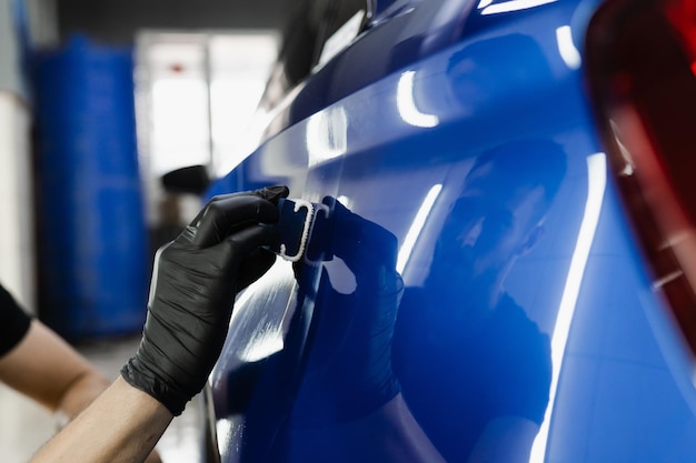 Proceso de aplicación de una capa protectora de cerámica en la carrocería del automóvil con una esponja para detallar el servicio de automóviles El trabajador del servicio de automóviles aplica una capa de cerámica para proteger la carrocería de los arañazos