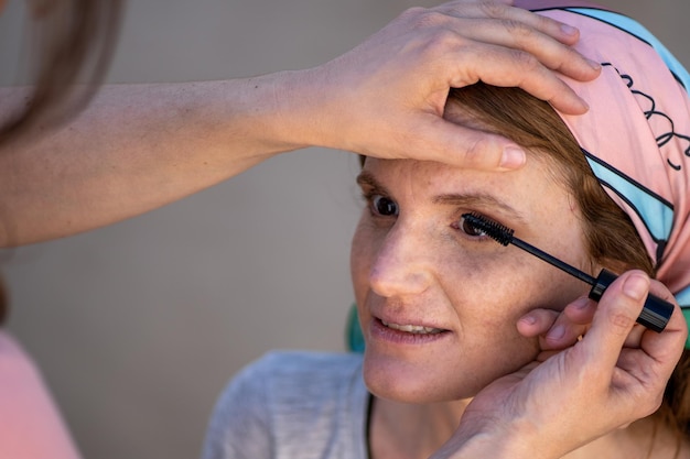 Proceso de aplicación de rímel a las pestañas de la mujer de mediana edad durante el maquillaje profesional