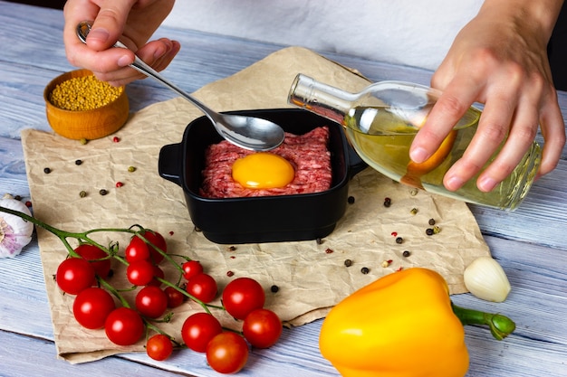 El proceso de cocinar chuletas en una mesa de madera clara de las manos femeninas de cerdo picada espolvorear temporada ...