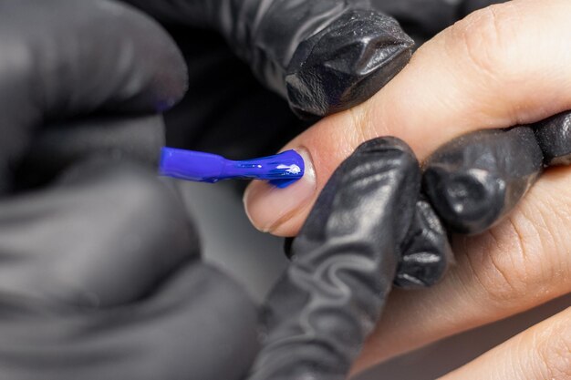 El proceso de creación de la manicura perfecta El manicurista pinta las uñas con esmalte de gel azul