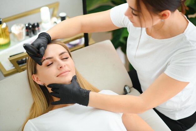 Proceso de creación de maquillaje permanente de cejas con una máquina en un salón de belleza