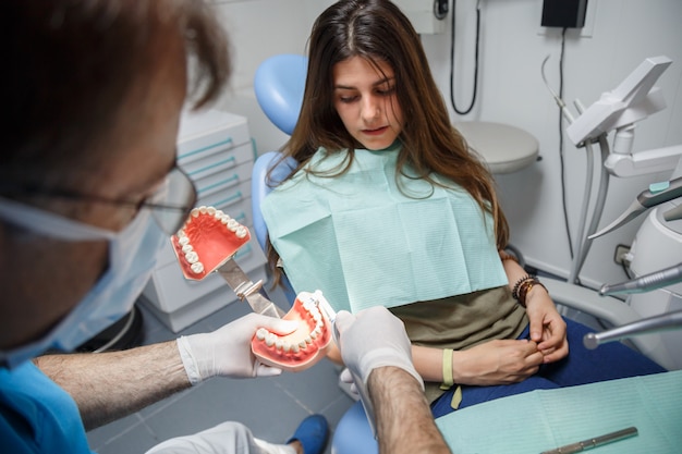 Proceso de demostración de médico profesional de cepillado de dientes sanos a joven mujer sentada en la silla.