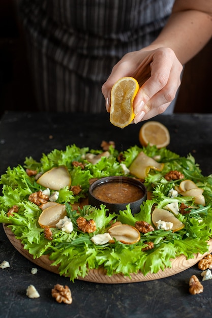 El proceso de elaboración de una ensalada light light con pera y queso azul. La mujer exprime el jugo del limón en la salsa de mostaza y miel.