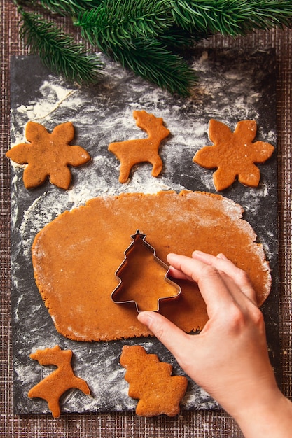 El proceso de elaboración de las galletas de jengibre navideñas. La mujer sostiene el molde en forma de árbol de Navidad en masa cruda para galletas de jengibre.