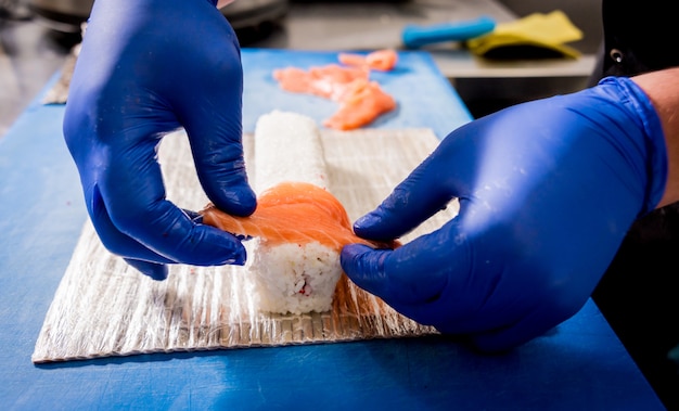 Proceso de elaboración de sushi y rollos en la cocina del restaurante. Chefs manos con cuchillo.