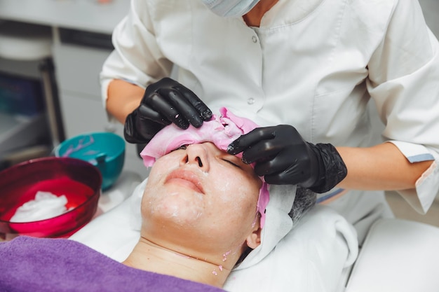 El proceso de eliminación de la máscara de alginato de la cara de una mujer Procedimiento de rejuvenecimiento facial Cuidado de la piel en un salón de belleza limpieza de la piel