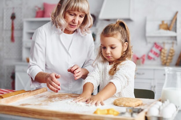 Proceso de enseñanza La abuela mayor con su nieta pequeña cocina dulces para Navidad en la cocina