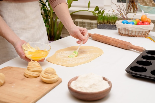 El proceso de extender la masa en casa sobre la mesa es de las manos de una mujer para hacer cruffins pasteles festivos para Pascua.