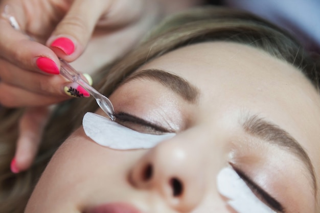 Proceso de extensión de pestañas a mujer joven linda en salón de belleza. El servicio al cliente en la habitación interior crea una imagen increíble. Asistente de creación de maquillaje de trabajo. Estilo de concepto, satisfacción cosmética. Copia espacio