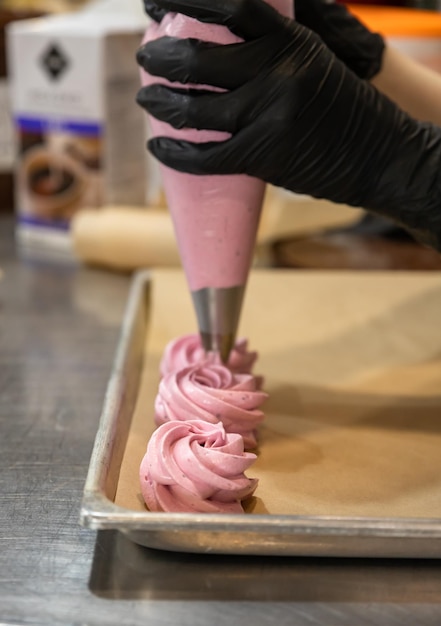 Proceso de fabricación de malvaviscos Chef exprimiendo el postre de merengue de una manga pastelera en una bandeja para hornear