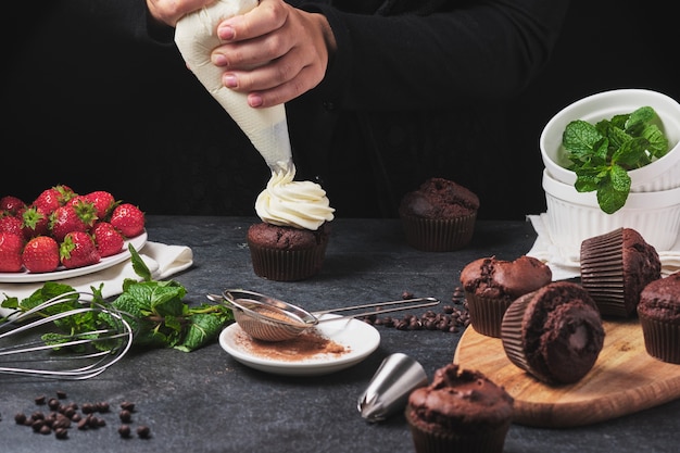 El proceso de hacer cupcakes. Manos del cocinero en el marco. Postre con nata, frutos rojos frescos, chocolate y menta. Muffins rellenos de ganache de chocolate.