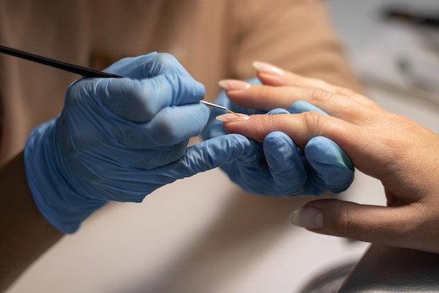 El proceso de hacer una manicura en un salón de spa. Manicurista aplica una base transparente en las uñas.