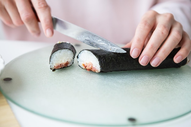 El proceso de hacer sushi la niña hace sushi con diferentes sabores salmón fresco caviar aguacate pepino jengibre arroz Cortar el rollo en pedazos Primer plano