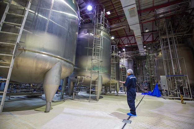 Proceso de inspección de trabajo masculino bodega de leche en polvo en la fábrica con tanques verticales de acero inoxidable