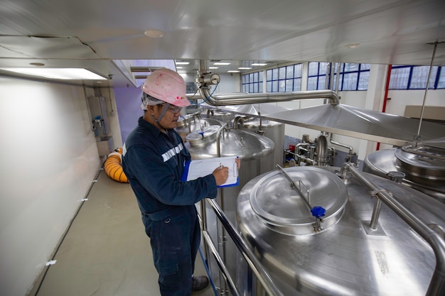 Proceso de inspección de trabajo masculino tanques de acero con tapa inoxidable con medidor de presión en la instalación del tanque del equipo para la bodega de agua en la fábrica con tanques verticales de acero inoxidable