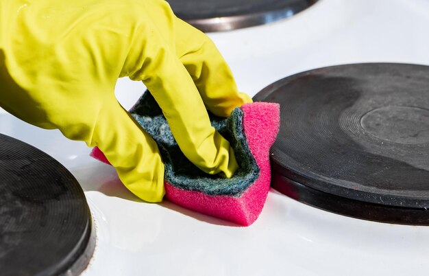 El proceso de lavado de una estufa eléctrica Una mano con un guante amarillo limpia la superficie blanca de la suciedad La limpieza de tareas