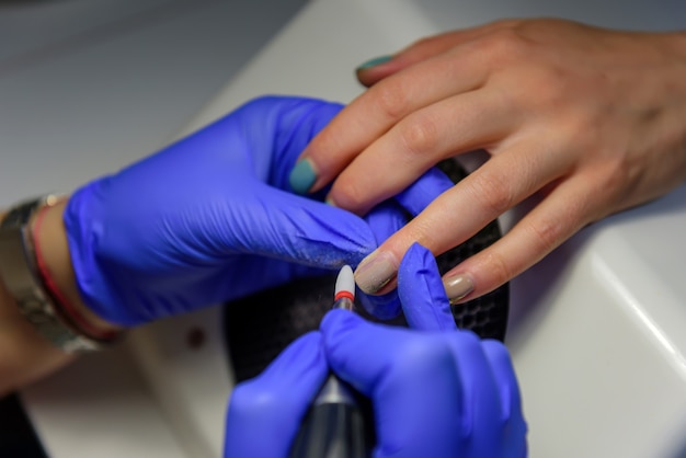 Proceso de limpieza de la uña del recubrimiento viejo, preparación antes de aplicar el esmalte de uñas. Manicure Master hace una manicura de hardware en guantes azules quitando el esmalte de gel en el salón