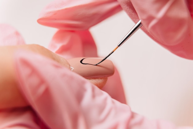 Foto proceso de manicura un maestro manicurista hace un dibujo sobre uñas artificiales usando barniz negro y un pincel fino