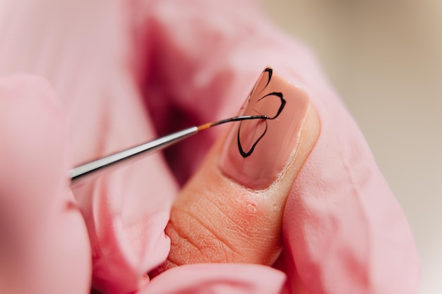 Foto proceso de manicura un maestro manicurista hace un dibujo sobre uñas artificiales usando barniz negro y un pincel fino