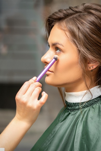 Proceso de maquillaje y peinado. Artista de maquillaje y peluquería preparando a joven mujer caucásica, trabajando en tándem.