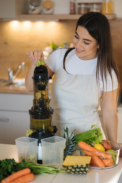 Foto proceso de mujer atractiva hacer jugo fresco en el exprimidor mujer en el delantal en la cocina