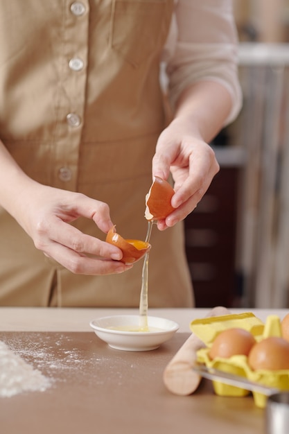 Proceso de mujer joven que separa la yema de huevo de la clara al hacer masa para pastelería