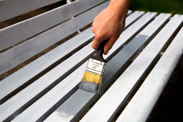 Proceso de pintura del banco de madera con pincel.