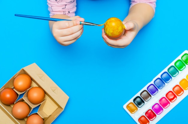 Foto en el proceso de preparación para la pascua, el niño pinta huevos de pascua con un pincel antes de las vacaciones. pinturas multicolores. copie el espacio.