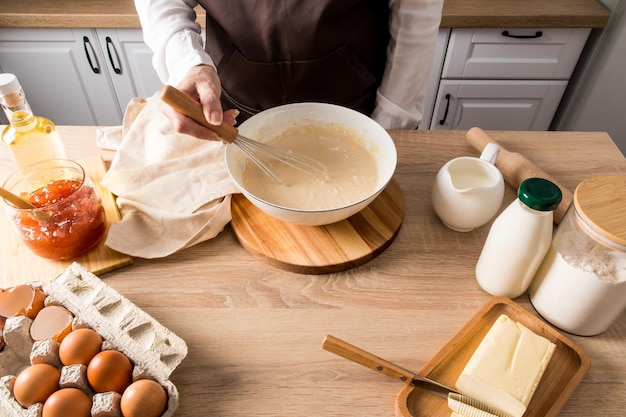 El proceso de preparar el desayuno en la cocina amasando la masa en un bol por el ama de casa en la encimera de la cocina con productos