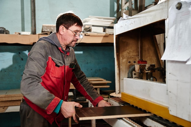 Proceso de producción y fabricación de muebles de madera en fábrica de muebles Trabajador carpintero hombre en monos procesa madera en equipo especial