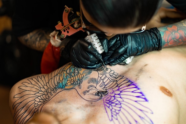 Proceso de salón de tatuajes. Una chica tatuadora rellenó un tatuaje. el proceso de rellenar un tatuaje en el cuerpo. Primer plano de las manos.