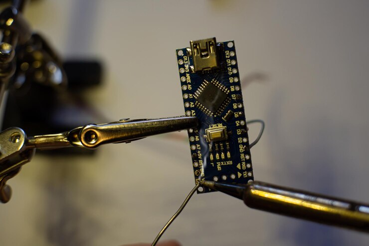 Foto el proceso de soldar cables a una placa arduino nano la abrazadera sujeta la placa con la mano
