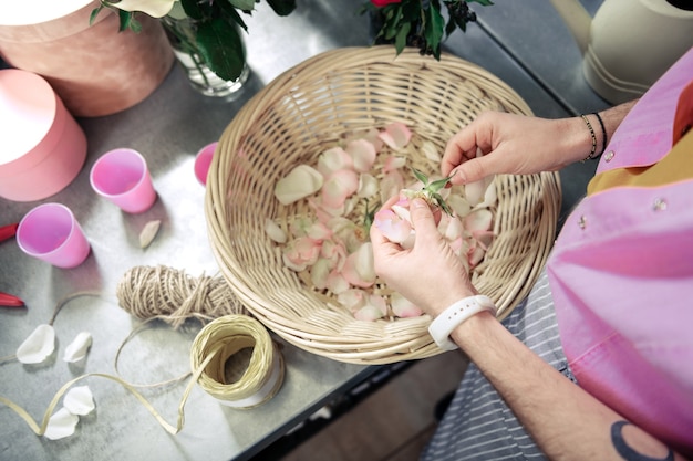 Proceso de trabajo. Floristería competente de pie en su lugar de trabajo y sosteniendo rosa