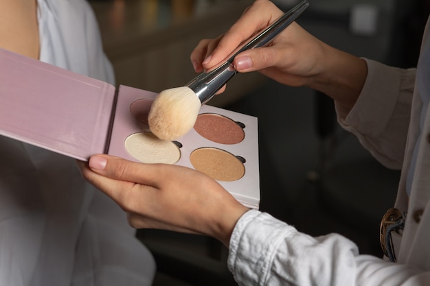 Proceso de trabajo: maquilladora que utiliza una paleta de resaltado y un pincel natural y maquilla a una mujer