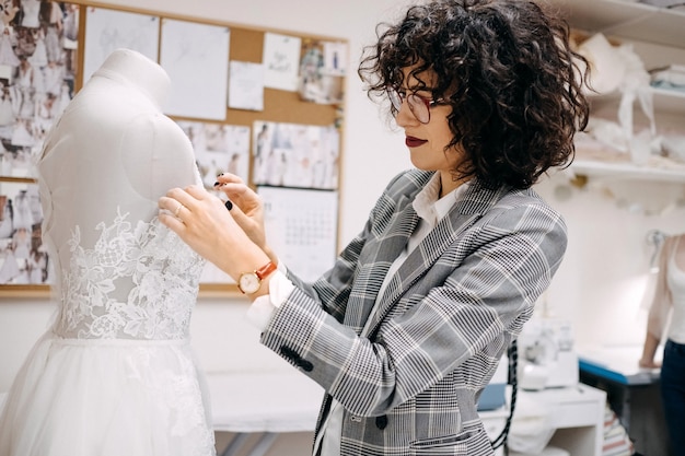 Proceso de trabajo de un sastre en su estudio Diseñador de moda coser vestido de novia sujetando encaje en maniquí