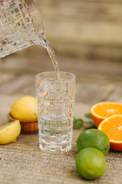 Proceso de verter agua fría en un vaso alto de cítricos frescos en la mesa naranja limón y lima alimentos