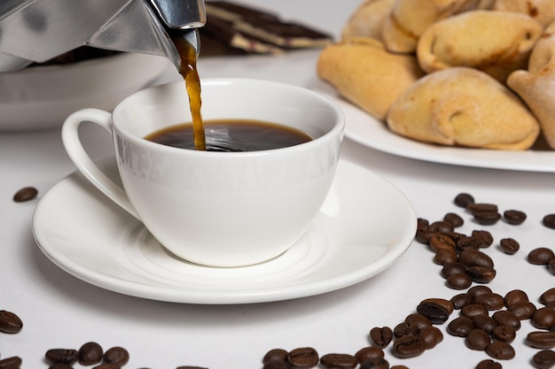 El proceso de verter café de una cafetera moka de géiser en una taza blanca